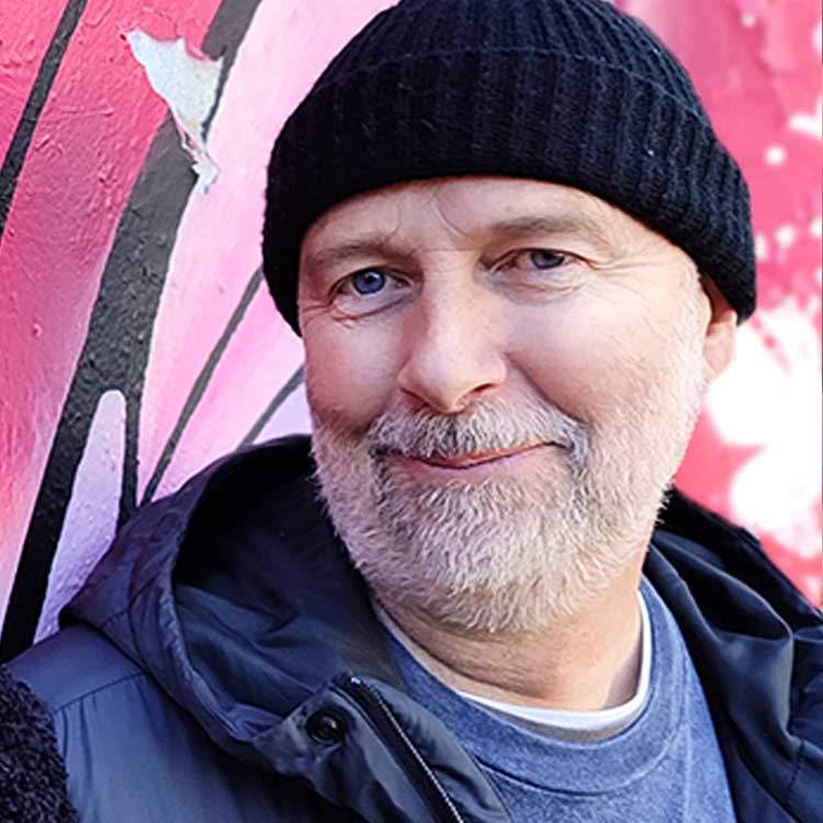 Portrait shot of Jeff West in front of a pink butterfly mural opens the About Jeff West page